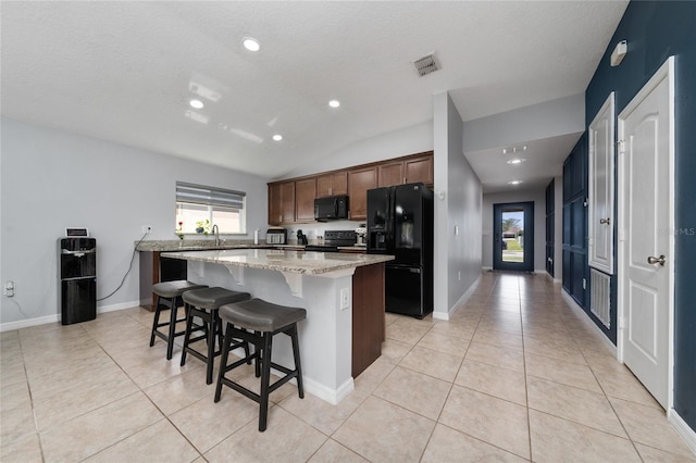 kitchen with black appliances, light tile patterned flooring, visible vents, and a center island