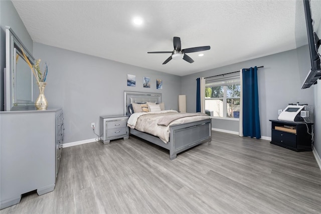 bedroom with light wood-style floors, a textured ceiling, and baseboards