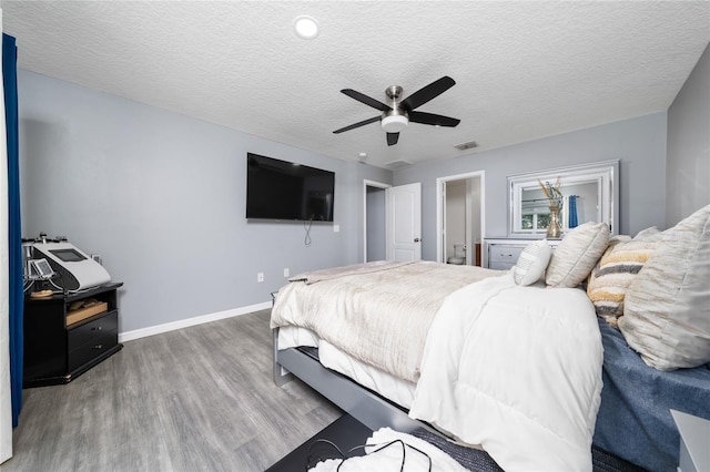 bedroom with a textured ceiling, ceiling fan, wood finished floors, visible vents, and baseboards