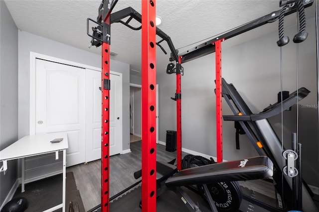 exercise room with baseboards, a textured ceiling, and wood finished floors