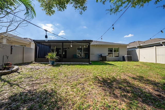 rear view of house with a yard, stucco siding, central AC unit, a sunroom, and a fenced backyard