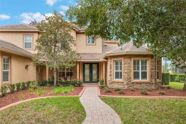 view of front of house featuring stone siding, stucco siding, a tiled roof, french doors, and a front yard