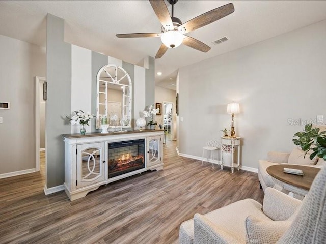 bar with visible vents, ceiling fan, wood finished floors, a lit fireplace, and baseboards