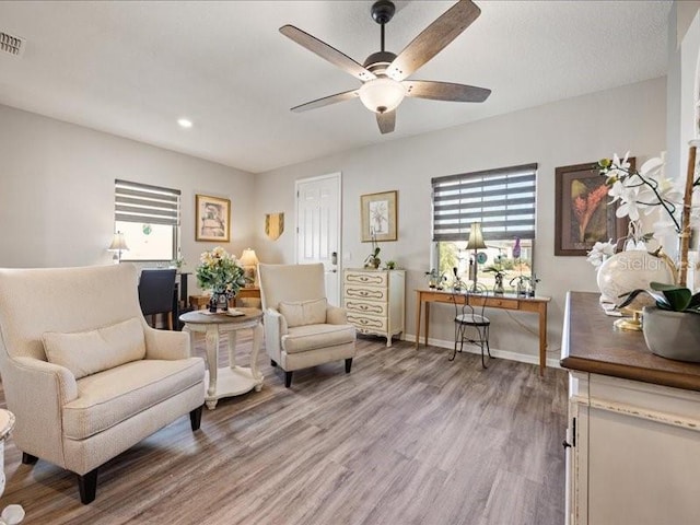 living area featuring visible vents, ceiling fan, baseboards, and wood finished floors