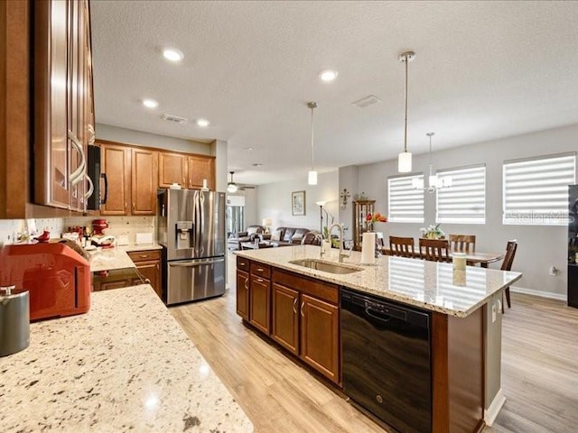 kitchen with light stone counters, stainless steel appliances, a sink, light wood-type flooring, and decorative light fixtures