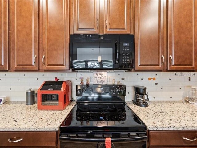 kitchen featuring brown cabinets, backsplash, black appliances, and light stone countertops