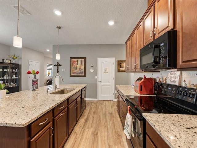 kitchen featuring visible vents, light wood-style floors, light stone counters, black appliances, and a sink