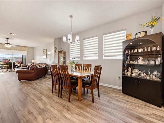 dining area featuring baseboards, visible vents, wood finished floors, and ceiling fan with notable chandelier