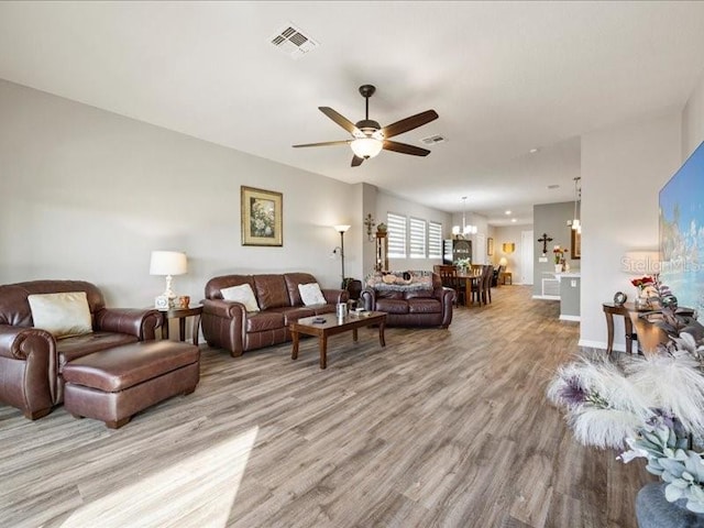 living room with light wood-type flooring, visible vents, and ceiling fan with notable chandelier