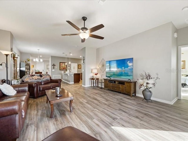 living room with ceiling fan with notable chandelier, baseboards, and wood finished floors