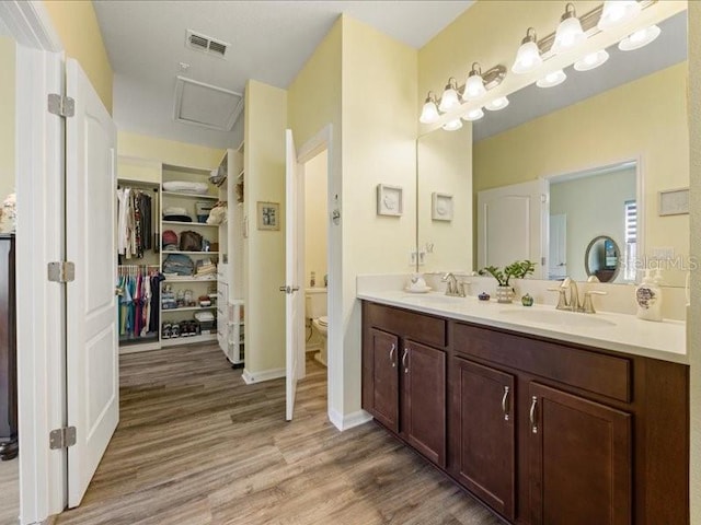 bathroom with toilet, wood finished floors, a sink, visible vents, and double vanity