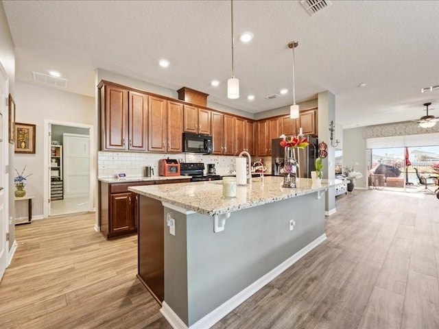 kitchen featuring light wood finished floors, black microwave, visible vents, and stove