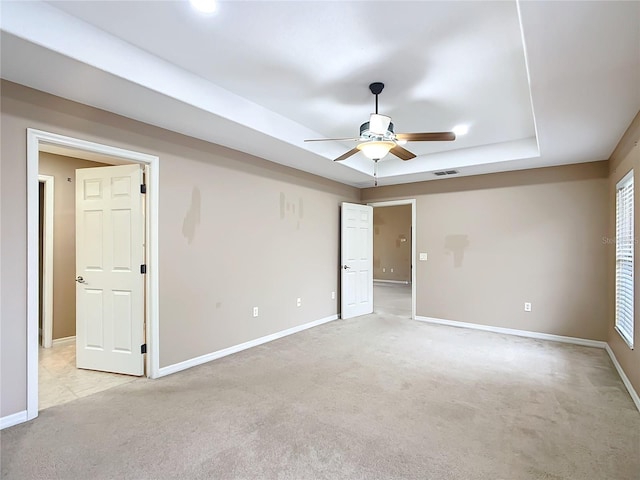 unfurnished room featuring baseboards, a tray ceiling, visible vents, and light colored carpet