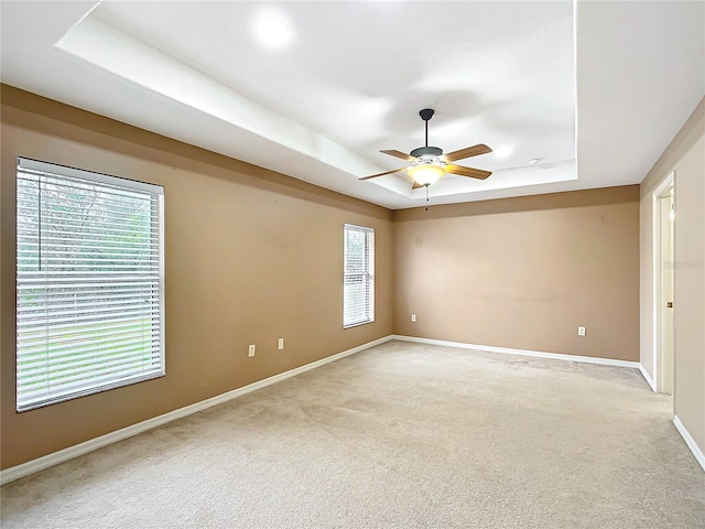 unfurnished room featuring light carpet, baseboards, a raised ceiling, and a ceiling fan