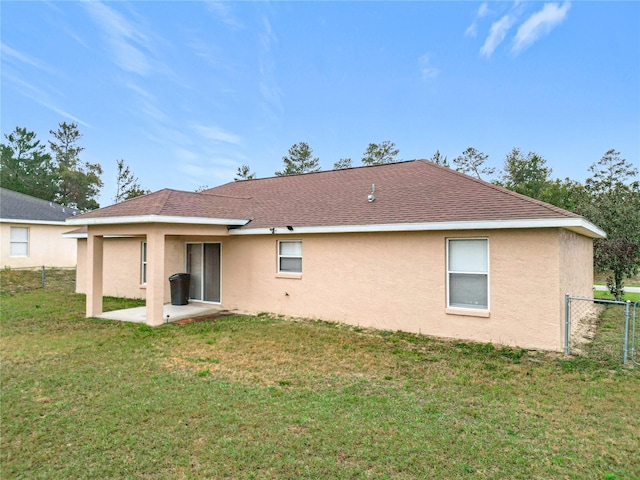 rear view of house with roof with shingles, a patio, a yard, stucco siding, and fence