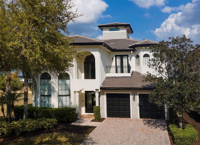 mediterranean / spanish-style house featuring decorative driveway, a balcony, a garage, and stucco siding