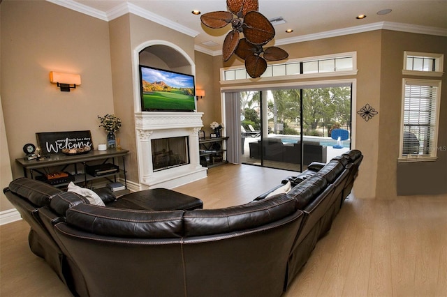 living room featuring a fireplace with raised hearth, a healthy amount of sunlight, ornamental molding, and wood finished floors