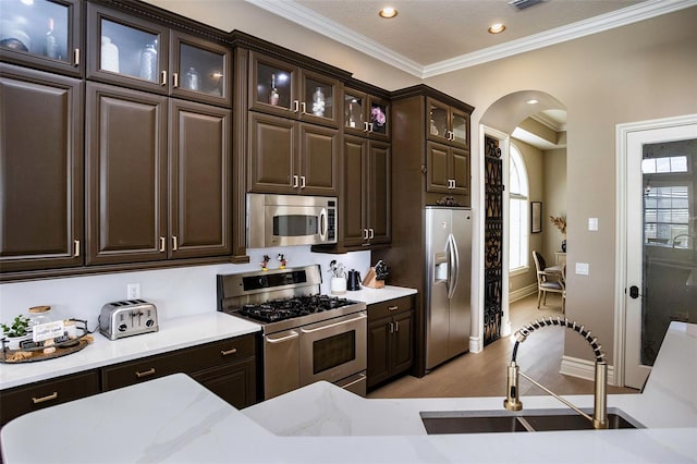 kitchen with a sink, arched walkways, dark brown cabinetry, appliances with stainless steel finishes, and light countertops