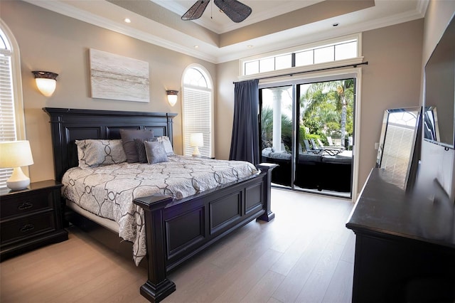 bedroom featuring access to exterior, crown molding, light wood-type flooring, a tray ceiling, and a ceiling fan