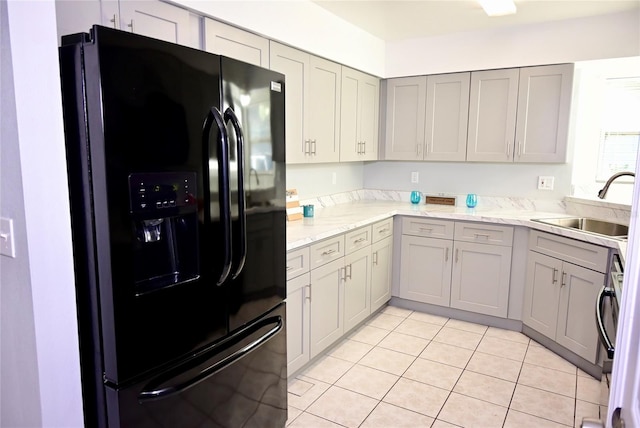 kitchen featuring light tile patterned flooring, a sink, black fridge with ice dispenser, gray cabinets, and light stone countertops