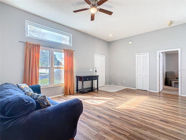 living room featuring a ceiling fan, a textured ceiling, baseboards, and wood finished floors