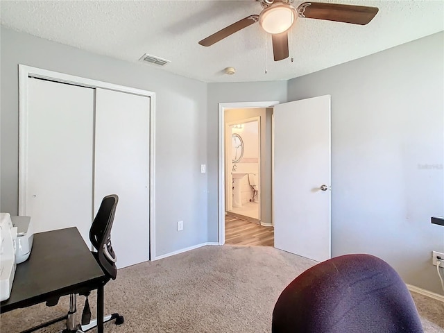 home office featuring a textured ceiling, carpet flooring, visible vents, baseboards, and a ceiling fan