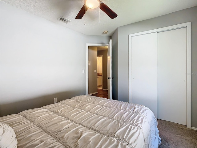 carpeted bedroom with a ceiling fan, a closet, visible vents, and a textured ceiling