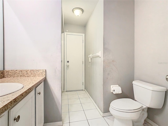 half bath with toilet, vanity, baseboards, and tile patterned floors