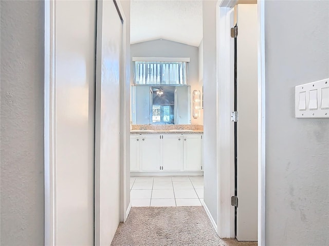 hall featuring vaulted ceiling, a textured wall, light tile patterned floors, and light colored carpet