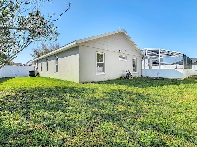 view of side of property featuring a lanai, central air condition unit, fence, and a lawn