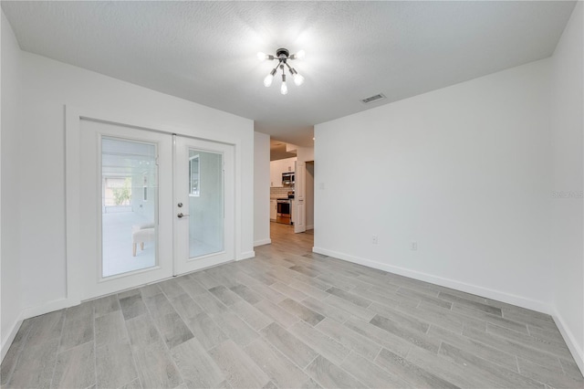 spare room featuring a textured ceiling, french doors, visible vents, and light wood-style floors