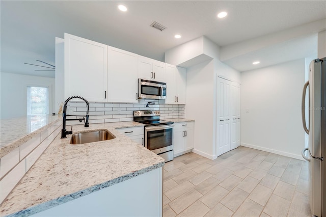 kitchen featuring light stone counters, stainless steel appliances, visible vents, backsplash, and a sink