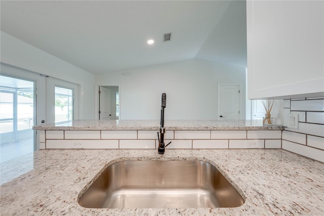 kitchen with light stone counters, lofted ceiling, visible vents, white cabinetry, and a sink