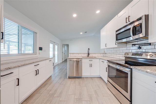 kitchen with stainless steel appliances, lofted ceiling, decorative backsplash, white cabinetry, and a sink