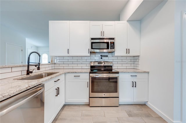 kitchen with appliances with stainless steel finishes, white cabinetry, a sink, and decorative backsplash