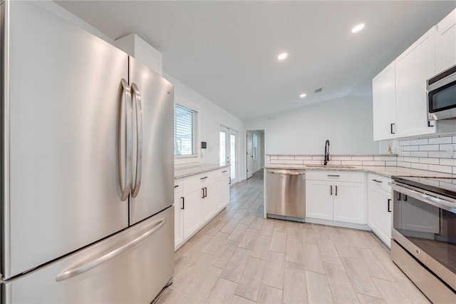 kitchen with backsplash, appliances with stainless steel finishes, vaulted ceiling, a sink, and light stone countertops