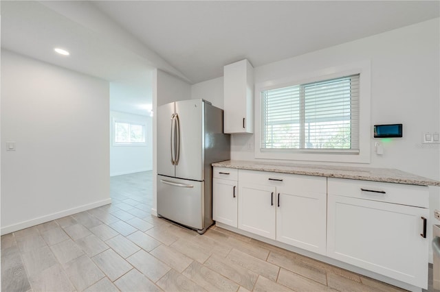 kitchen featuring light stone countertops, white cabinetry, and freestanding refrigerator