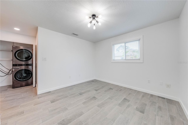 empty room with baseboards, light wood-style flooring, visible vents, and stacked washer / drying machine