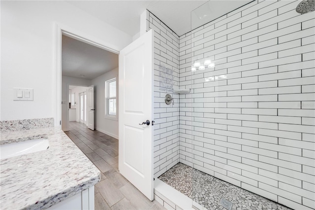 bathroom with wood tiled floor, a tile shower, and vanity