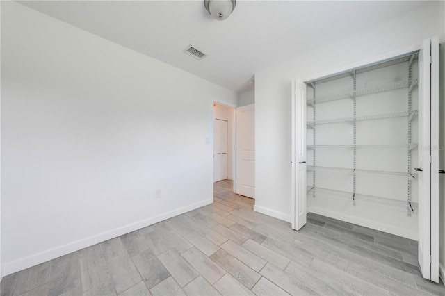 unfurnished bedroom with a closet, wood finished floors, visible vents, and baseboards