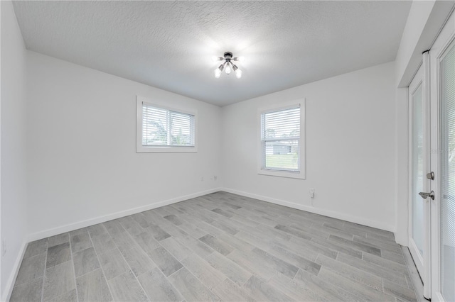 spare room with a textured ceiling, light wood finished floors, and baseboards