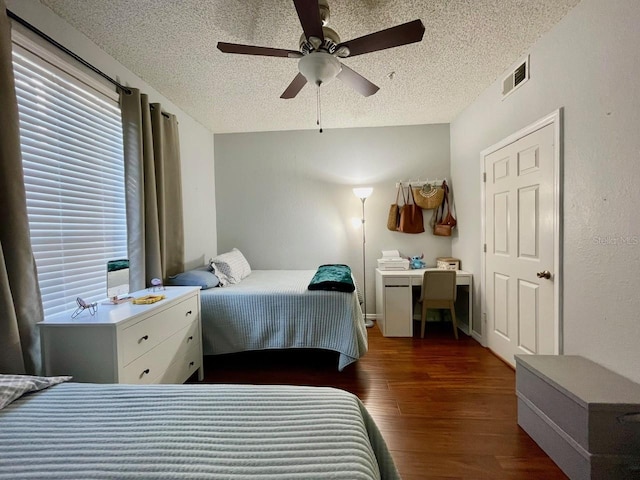 bedroom with a textured ceiling, ceiling fan, dark wood-style flooring, visible vents, and baseboards