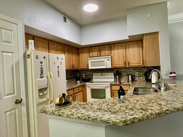 kitchen featuring white appliances, visible vents, a peninsula, a sink, and backsplash