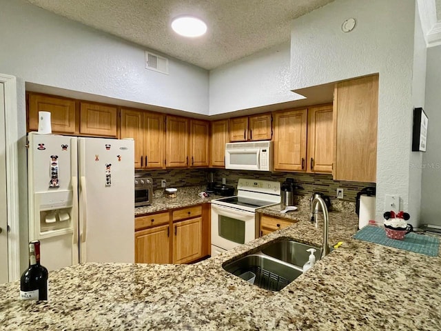 kitchen featuring white appliances, tasteful backsplash, visible vents, light stone counters, and a sink