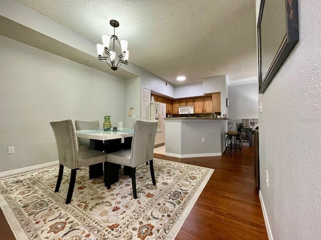 dining room with baseboards, a textured ceiling, a chandelier, and wood finished floors