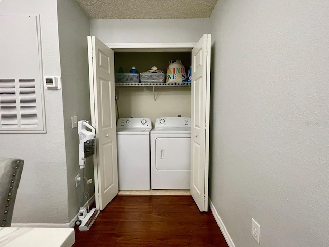 clothes washing area with dark wood-style floors, washer and clothes dryer, a textured ceiling, laundry area, and baseboards