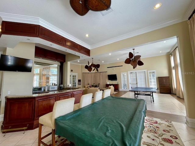 rec room featuring a ceiling fan, visible vents, crown molding, and light tile patterned floors