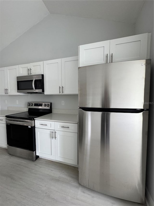 kitchen with stainless steel appliances, white cabinetry, vaulted ceiling, light countertops, and light wood-type flooring