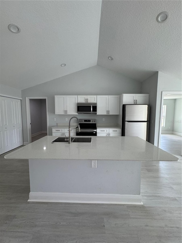 kitchen with white cabinets, a spacious island, appliances with stainless steel finishes, vaulted ceiling, and a sink