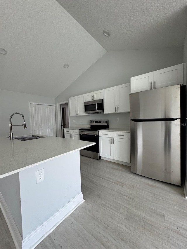 kitchen with a sink, white cabinetry, vaulted ceiling, appliances with stainless steel finishes, and light wood-type flooring